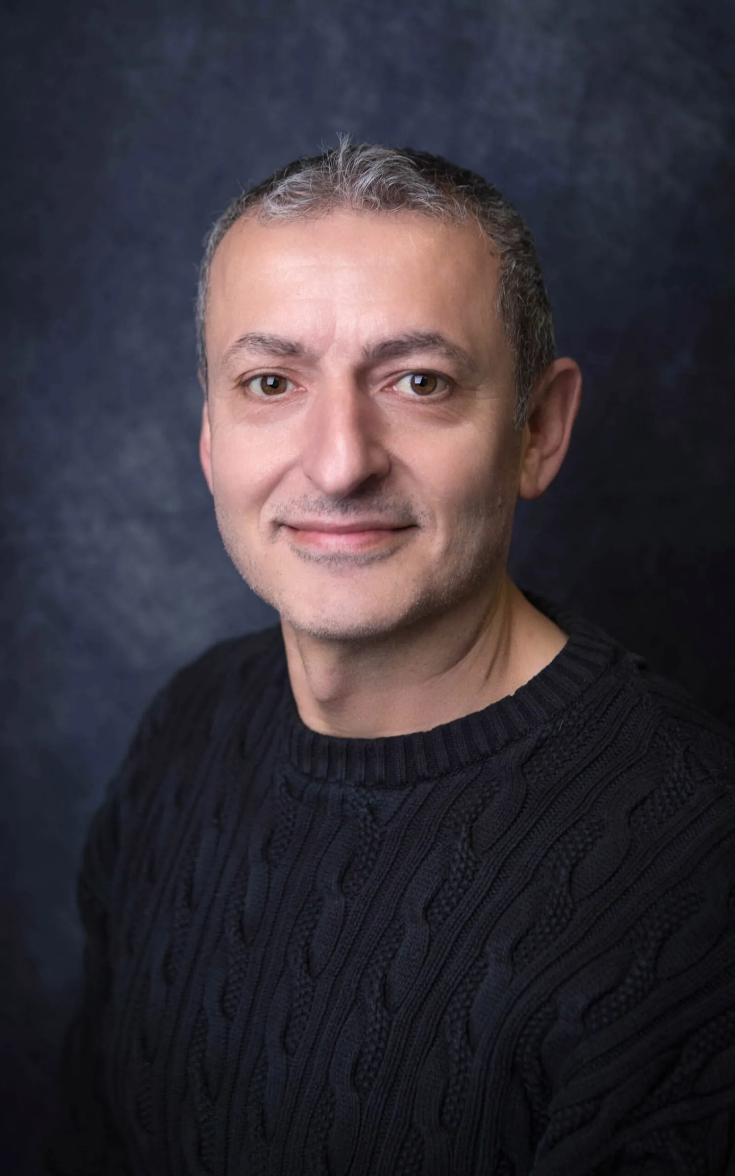 Hayri Evmez in einem schwarzen Oberteil vor einem dunklen Hintergrund.